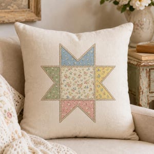 May include: A square off-white throw cushion featuring a central eight-pointed star design. The star is composed of five distinct sections, each decorated with a small floral pattern in shades of blue, green, yellow, pink, and cream.
