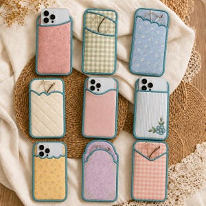 May include: Nine rectangular fabric phone pouches with teal trim, featuring various patterns including pink floral, green gingham, blue floral, cream quilted, solid pink, blue striped with floral embroidery, yellow floral, purple damask, and pink gingham.