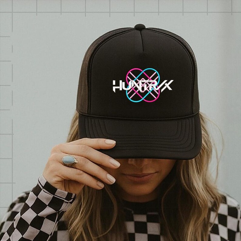 Puede incluir: Gorra de camionero negra con parte trasera de malla y visera curva. La gorra presenta la palabra "HUNGRX" en blanco, con un dise&ntilde;o rosa y azul superpuesto. La persona lleva una camisa a cuadros blancos y negros.