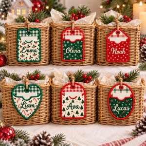 May include: Six square woven wicker baskets filled with white tissue paper, evergreen sprigs, and red berries. Each basket features a hanging fabric tag with a unique holiday pattern and a personalized name: Emma, Olivia, Noah, Liam, Ava, and Lucas.