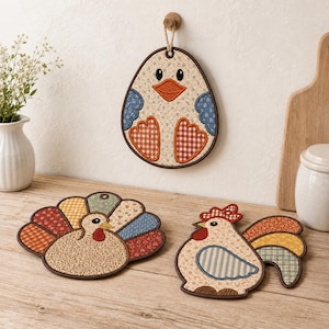 May include: Three fabric-covered decorative wall hangings and trivets shaped like a duck, a turkey, and a rooster. Each piece features a mix of floral, gingham, and plaid patterns in blue, orange, red, and yellow tones with dark brown trim edges.