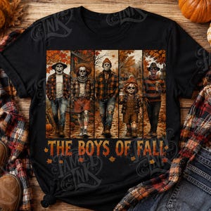 May include: A black t-shirt featuring a graphic print of five horror movie characters dressed in autumn clothing walking through a forest. The text THE BOYS OF FALL is printed in orange below the characters, surrounded by scattered orange maple leaves.