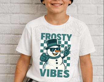 Może przedstawiać: Biały t-shirt z krótkim rękawem z grafiką bałwana w cylindrze i okularach przeciwsłonecznych, wykonującego znak pokoju i wskazującego palcem. Wzór zawiera niebiesko-zielone tło w kratkę oraz napis FROSTY VIBES wykonany niebiesko-zielonymi literami.