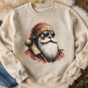 May include: A cream-colored crewneck sweatshirt featuring a graphic print of Santa Claus wearing a red hat, a tan beanie with a logo patch, and dark sunglasses. Santa has a long white beard and is dressed in a red jacket with a fur-lined collar.