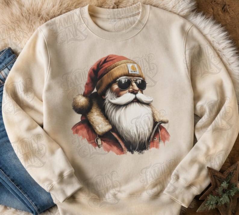 May include: A cream-colored crewneck sweatshirt featuring a graphic print of Santa Claus wearing a red hat, a tan beanie with a logo patch, and dark sunglasses. Santa has a long white beard and is dressed in a red jacket with a fur-lined collar.