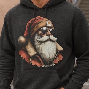 May include: A dark charcoal gray hooded sweatshirt featuring a graphic print of a bearded figure wearing a red Santa hat, a tan beanie, and dark sunglasses. The figure has a long white beard and wears a red jacket with a tan fur-lined collar.
