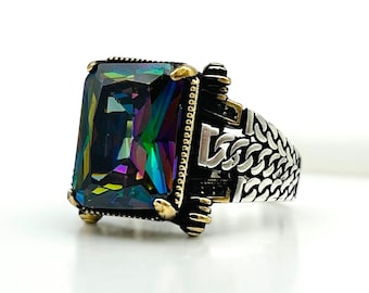 May include: A silver ring with a large, rectangular, iridescent gemstone. The gemstone displays a spectrum of colors, including green, blue, and purple. The ring has a detailed, textured band with gold accents, creating a striking contrast.