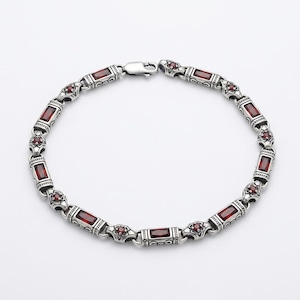 Peut inclure: Un bracelet en m&eacute;tal argent&eacute; compos&eacute; de maillons rectangulaires et circulaires altern&eacute;s. Les maillons rectangulaires sont sertis de pierres rouges fonc&eacute;es taille baguette, tandis que les maillons circulaires contiennent de petites pierres rouges.