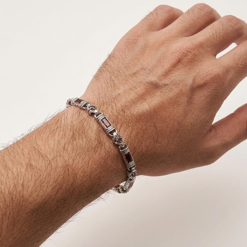 Peut inclure: Un bracelet &agrave; maillons en m&eacute;tal argent&eacute; orn&eacute; d'incrustations de pierres pr&eacute;cieuses rectangulaires rouge fonc&eacute;. Le bracelet est compos&eacute; de segments m&eacute;talliques travaill&eacute;s alternant avec des pierres lisses de couleur rouge profond.