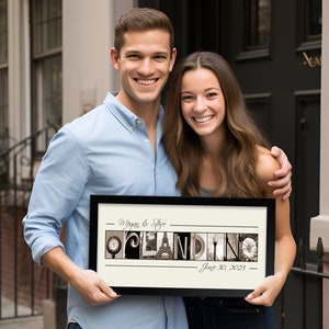 May include: A framed print with the word "OPLANDING" spelled out in sepia-toned letters, with the date "June 30, 2023" below. The print is held by a smiling couple. The frame is black.