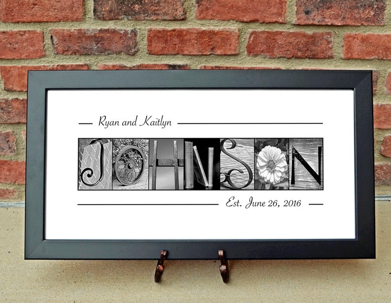 May include: Black framed print with the name "JOHNSON" spelled out in black and white images. The names "Ryan and Kaitlyn" and the date "Est. June 26, 2016" are above and below the name.