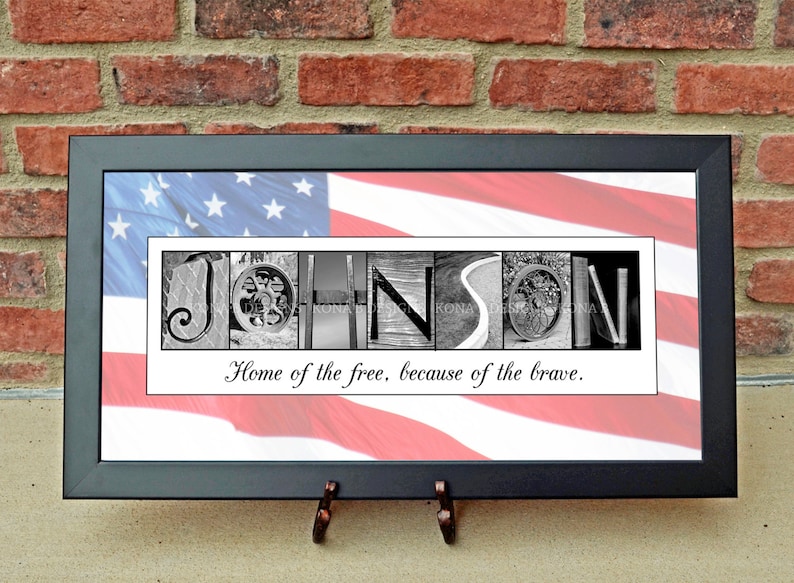 May include: Framed artwork featuring the name "JOHNSON" spelled out in black and white images. The background is an American flag. The text "Home of the free, because of the brave" is below the name. The frame is black.