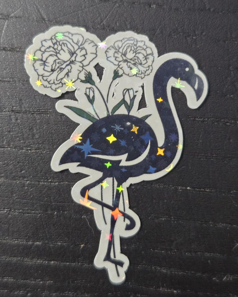 May include: A sticker featuring a stylized flamingo with a dark blue body and a constellation design. The flamingo holds two white flowers. The sticker has a holographic, iridescent effect.