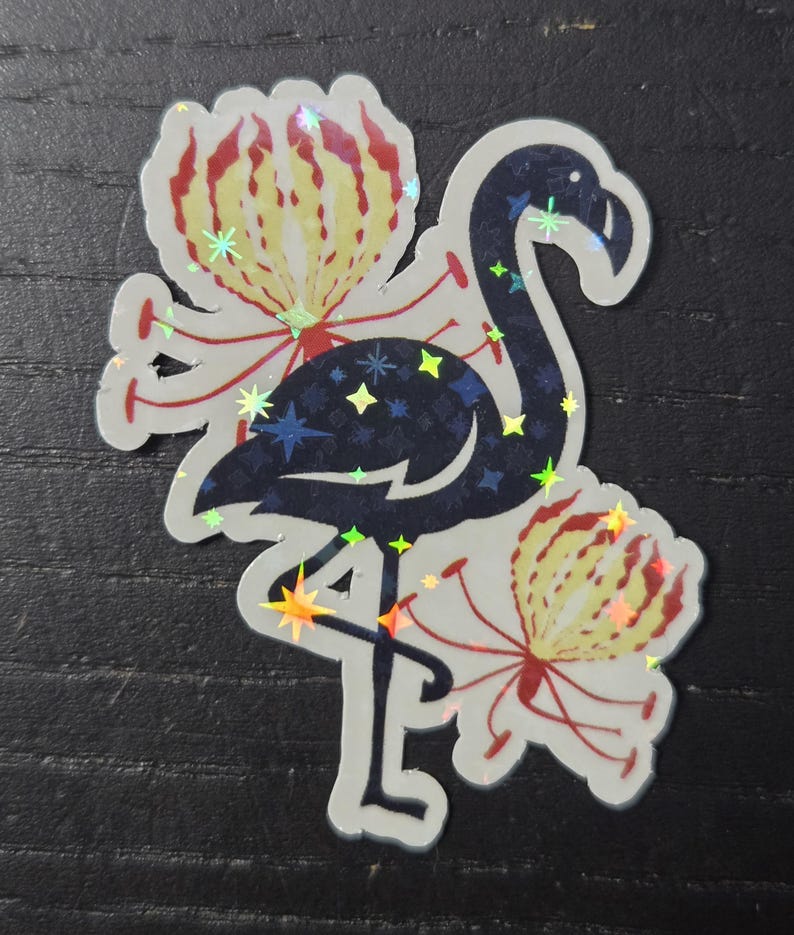 May include: A sticker featuring a stylized flamingo with a dark blue body and iridescent star accents. The flamingo is surrounded by two flowers with yellow and red petals. The sticker has a holographic finish.