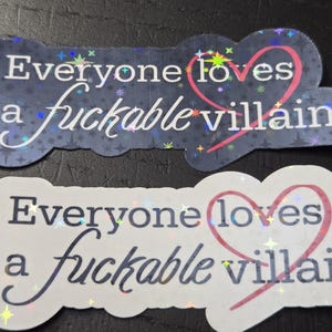 May include: Two stickers with the phrase "Everyone loves a fuckable villain." One sticker is dark blue with a starry background, the other is white. Both have a pink heart.