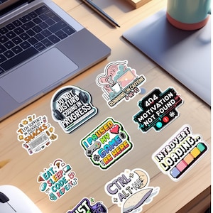 Op de afbeelding: Een verzameling kleurrijke stickers met tech- en gamingthema's, met slogans als "Do Not Disturb Coding in Progress", "I Paused My Game to Be Here" en "Just One More Level". Een laptop, koffiekopjes en een muis zijn ook zichtbaar.