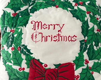 May include: A white Christmas pillow with a green holly wreath design and red berries. The words "Merry Christmas" are embroidered in red. A large red bow is at the bottom of the pillow.