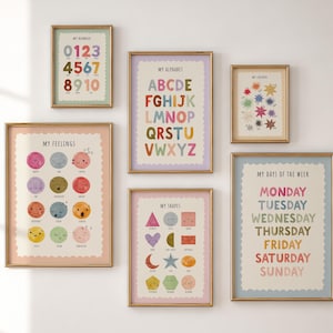 May include: A set of six educational wall art prints in gold frames featuring colourful illustrations of numbers, the alphabet, colours, feelings, shapes, and days of the week with text labels for each item, arranged in a gallery wall display.