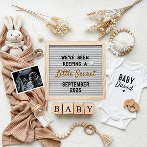 Könnte beinhalten: Eine Babyankündigung mit einem Buchstabenbrett mit der Aufschrift "We've been keeping a Little Secret September 2025". Ein Ultraschallbild, ein weißer Body mit "Baby David" und Holzblöcke mit "BABY" sind ebenfalls zu sehen.