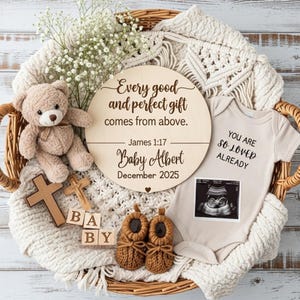 Puede incluir: Un anuncio de bebé en una cesta de mimbre. Incluye un letrero de madera con texto, un osito de peluche, una cruz, patucos de bebé y un body con una imagen de ultrasonido. El letrero dice "Every good and perfect gift comes from above."