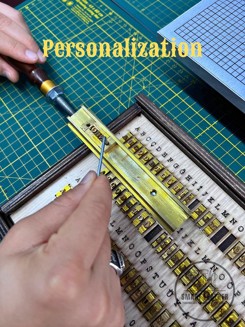 K&ouml;nnte beinhalten: Nahaufnahme eines Metallpr&auml;gewerkzeugs mit Holzgriff und Messing-Schrifttr&auml;ger. Der Text "Personalisierung" ist gelb dargestellt. Das Werkzeug ist mit einzelnen Buchstabenstempeln ausgestattet.