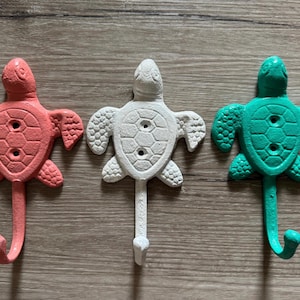 May include: Three turtle-shaped hooks in coral, white, and teal colors. Each hook has a detailed shell design and a curved hook for hanging items.
