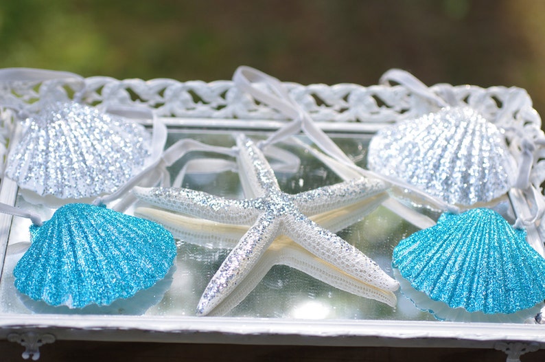 May include: Four decorative seashells, two blue and two silver, with a glittery white starfish on a white tray.