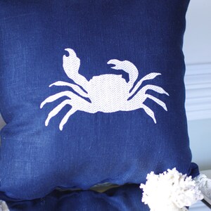 May include: A blue throw pillow with a white embroidered crab design.