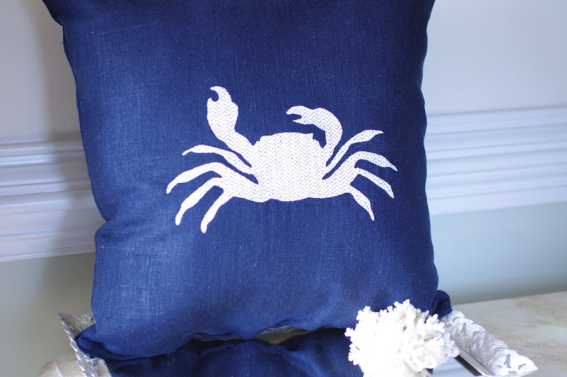 May include: A blue throw pillow with a white embroidered crab design.