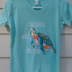 May include: A turquoise blue v-neck t-shirt with a sea turtle graphic and the text "Saltwater Heals Everything".