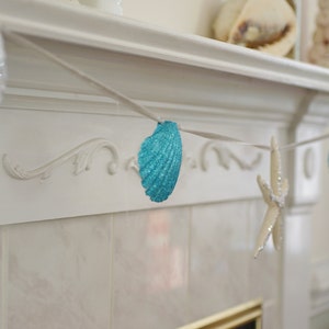 May include: A white fireplace mantel decorated with a blue and white seashell garland. The garland is strung with blue seashells and a white starfish.