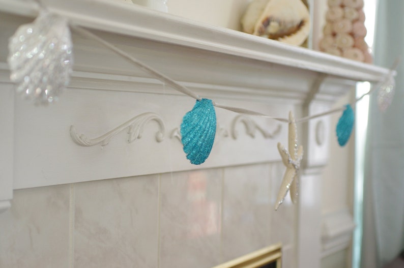 May include: A white fireplace mantel decorated with a blue and white seashell garland. The garland is strung with blue seashells and a white starfish.