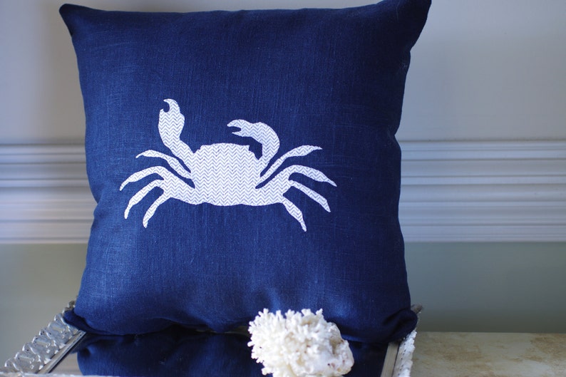 May include: A navy blue throw pillow with a white crab design. The crab is outlined in white and has a chevron pattern inside.
