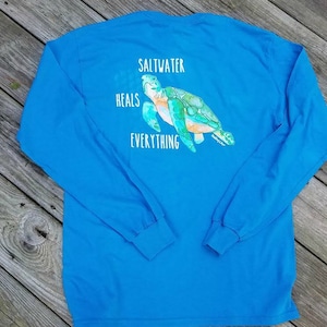 May include: A blue long-sleeved t-shirt with a sea turtle graphic and the text "Saltwater Heals Everything".