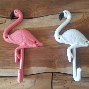 May include: Two cast iron flamingo hooks, one pink and one white, with black beaks. The hooks are designed to be mounted on a wall and add a tropical touch to any space. The flamingo hooks are a decorative and functional item.