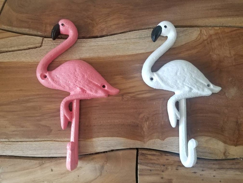May include: Two cast iron flamingo hooks, one pink and one white, with black beaks. The hooks are designed to be mounted on a wall and add a tropical touch to any space. The flamingo hooks are a decorative and functional item.