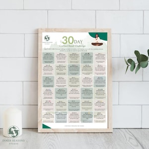 May include: A framed print titled "30 Day Cortisol Reset Challenge" with a light wood frame. The print features a grid of daily practices, a logo, and the text "Inner Seasons Studio". A white candle and a plant are in the foreground.