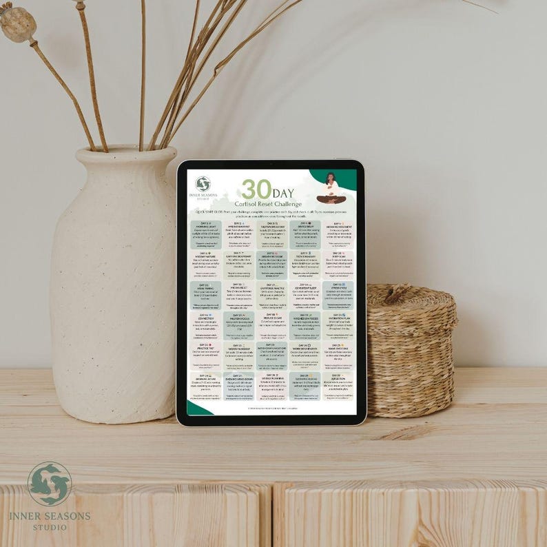 May include: A digital tablet displays a 30-day cortisol reset challenge. The screen features a green and white design with daily tasks and the text "Inner Seasons Studio." The tablet rests on a wooden surface, next to a white vase with dried stems and a woven basket.