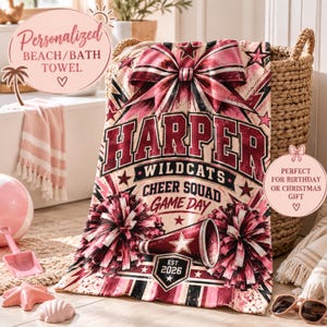 May include: A rectangular beach or bath towel featuring a cheerleading theme with a large pink bow at the top. The text reads HARPER, WILDCATS, CHEER SQUAD, GAME DAY, and EST. 2026. The design includes maroon and pink pom-poms and a megaphone graphic.