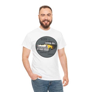 May include: White t-shirt featuring a graphic of a classic car with yellow flames and the text "BORN to Drive Classics" inside a gray circle. The car is black and yellow. The shirt is being worn by a person.