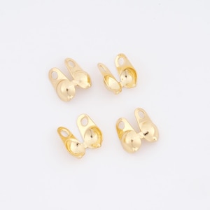May include: Several small, gold-colored jewelry findings are arranged on a white surface. Each finding has a rounded base with a small loop and a curved, open top. The findings appear to be new and unused.