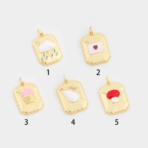 Pode incluir: Cinco pingentes dourados com vários desenhos. Um pingente apresenta uma nuvem com chuva, outro um envelope com um coração, um cupcake, uma concha e um cogumelo. Cada pingente tem uma borda decorativa.