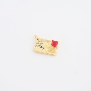 May include: A gold-colored pendant in the shape of a postcard. The pendant has the words "Love Always" in cursive and a square, red gemstone. The pendant is on a white background.