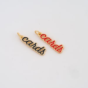 May include: Two gold-toned metal charms shaped like the word cards in cursive script. One charm features black enamel inlay, while the other charm features red enamel inlay. Each charm includes a small jump ring at the top for attachment.