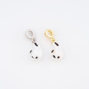May include: Two charm pendants, one silver-toned and one gold-toned, each featuring a white, teardrop-shaped design with black spots. The pendants have a loop at the top for attaching to a bracelet or necklace. The charms are on a white background.
