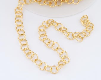 May include: A close-up of a gold-colored chain with a series of connected circular links. The chain is coiled in a roll and also laid out in a curved line. The chain is on a white background.