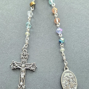 May include: A rosary with colorful faceted beads and silver-toned metal components. The cross features a detailed depiction of Jesus, and the other end has a pendant with a religious image and the words "Guardian Angel."