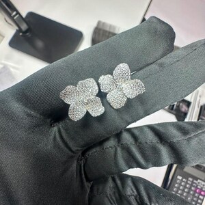 May include: A pair of silver-toned stud earrings, each shaped like a four-petaled flower. The surface of the petals is densely covered in small, clear, reflective stones that create a sparkling, textured appearance across the entire floral design.