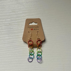 May include: Rainbow-colored chainmail earrings with gold-colored ear wires. The earrings are attached to a brown tag that reads "Handmade with Love". The earrings feature a series of colorful interlocking rings.