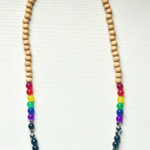 Könnte beinhalten: Eine Halskette mit Holzperlen und einem Regenbogen aus farbigen Perlen. Die Halskette geht in schwarze Perlen mit silberfarbenen Akzenten über. Die Perlen sind auf einer Schnur aufgefädelt und bilden ein stilvolles Accessoire.
